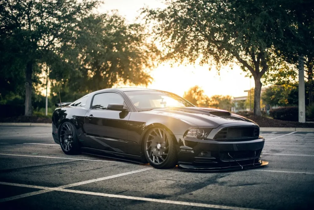 Carro esportivo preto, um Ford Mustang GT, estacionado em um estacionamento durante o pôr do sol.