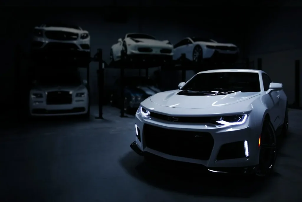 Carro esportivo branco, um Chevrolet Camaro ZL1, em uma garagem com outros carros de luxo.