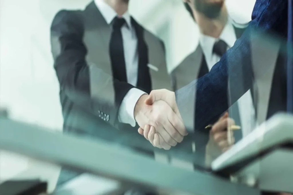 Empresários em trajes formais apertando as mãos, simbolizando negociação de consórcio contemplado.