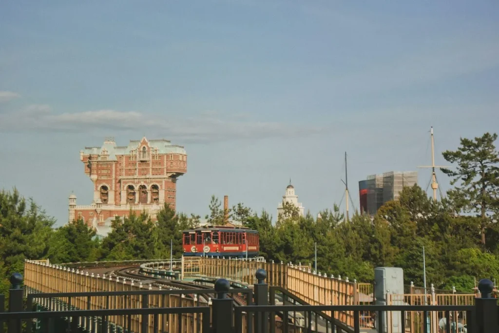 Vista panorâmica da Tokyo DisneySea com a atração Tower of Terror em destaque, um trem vermelho passando na frente e a paisagem arborizada do parque.