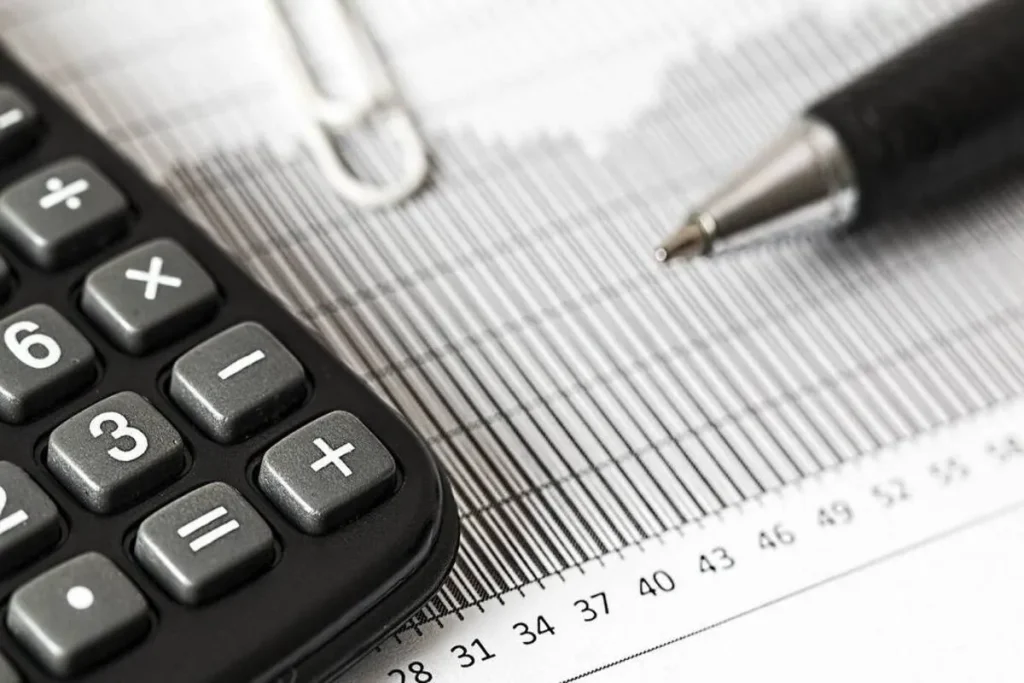 Uma calculadora e uma caneta sobre um documento financeiro, representando a tarefa de calcular impostos e taxas, como o IOF (Imposto sobre Operações Financeiras). A imagem transmite o conceito de contabilidade e planejamento financeiro.