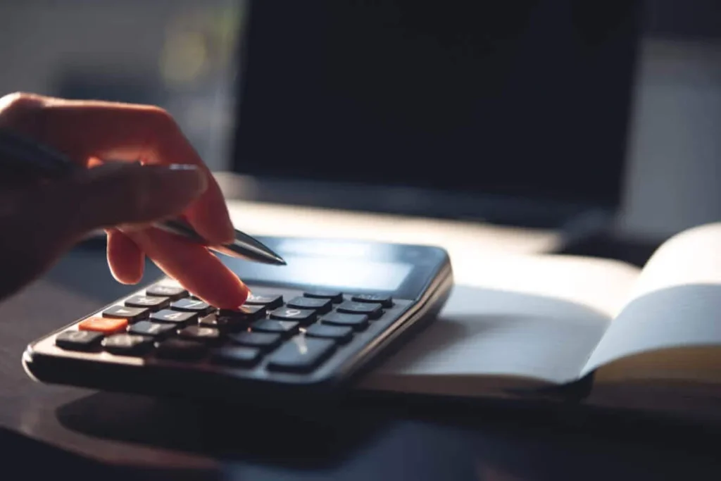 Pessoa usando calculadora com caderno ao lado, representando planejamento e autofinanciamento.