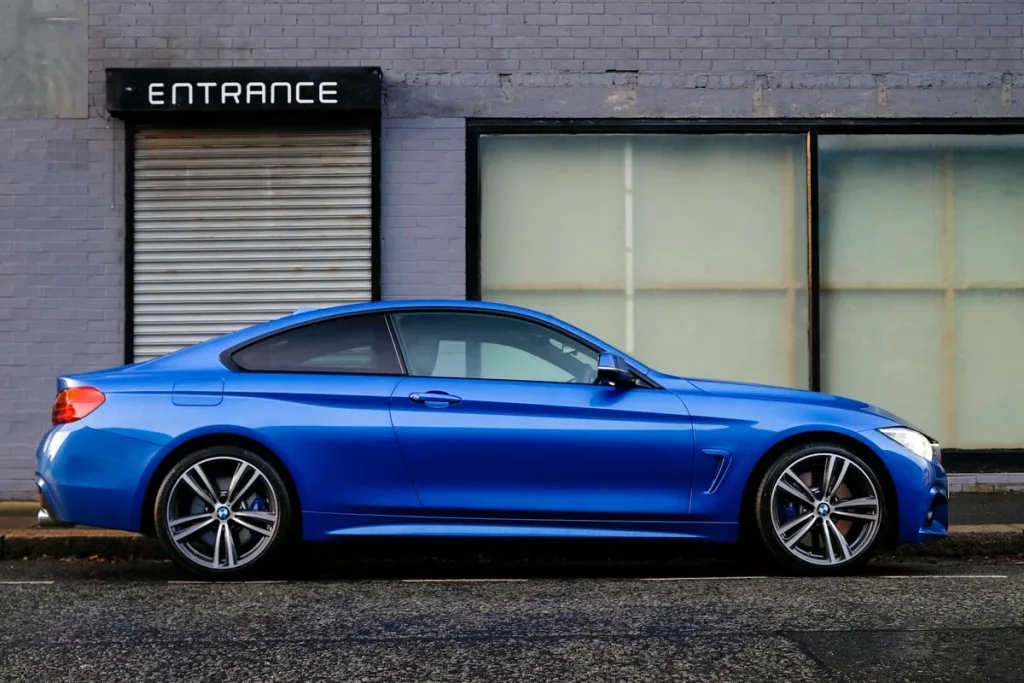 Um carro esportivo azul brilhante estacionado na rua, com a parede de tijolos de um prédio no fundo.