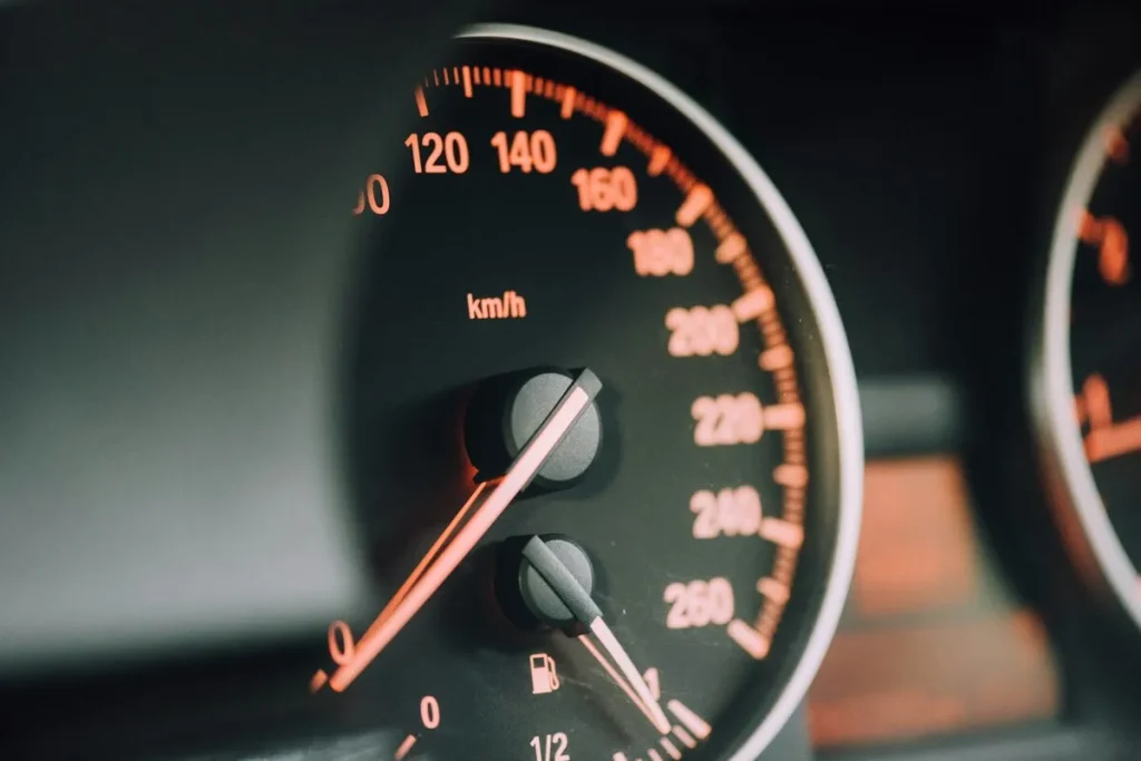 Close-up do velocímetro de carro moderno marcando alta velocidade em km/h (quilômetros por hora) com iluminação laranja/âmbar, sugerindo performance, risco ou urgência de compra.