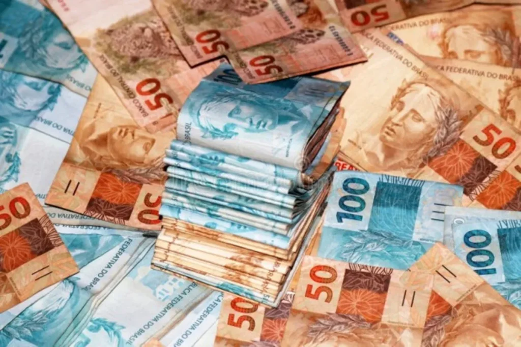 Muitas notas de 50 e 100 Reais (BRL) empilhadas e espalhadas, representando o montante de dinheiro e crédito de 100 mil reais em um consórcio.