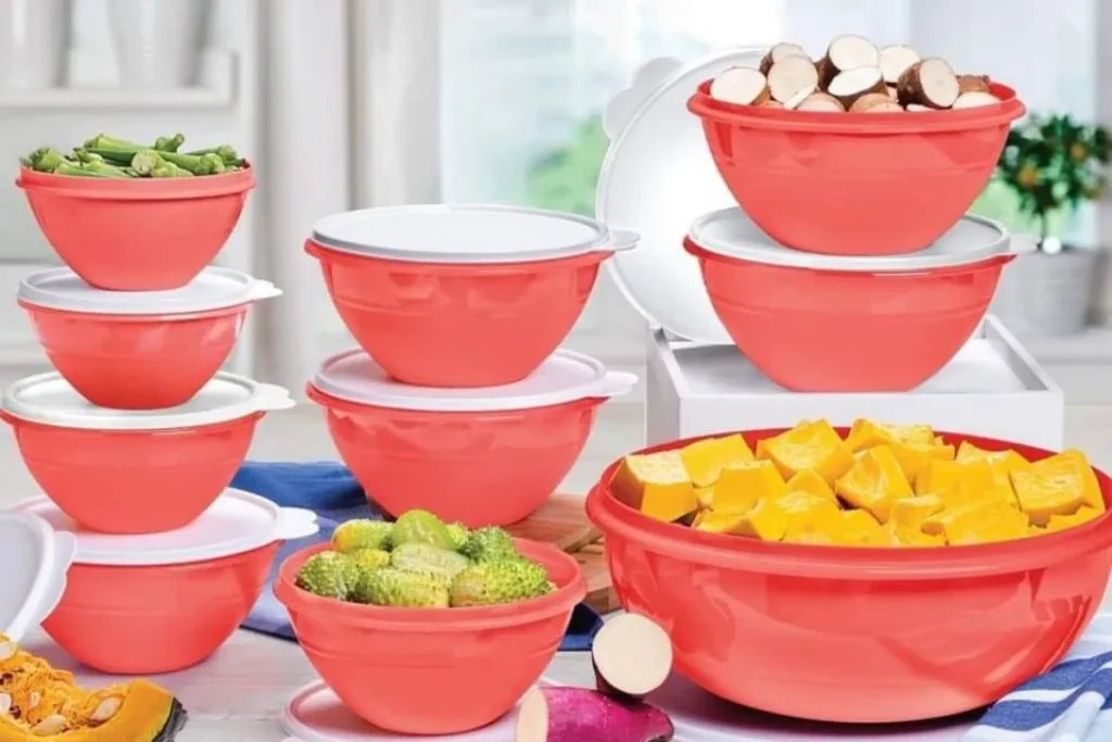 Variedade de potes Tupperware vermelhos e brancos cheios de legumes frescos, representando produtos para o lar em um consórcio.