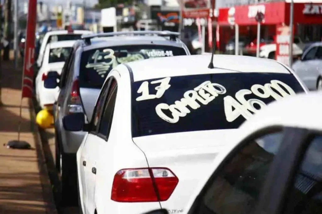 Fila de carros usados brancos em revenda com cartazes de "Vende-se" nos vidros, simbolizando a compra por consórcio.