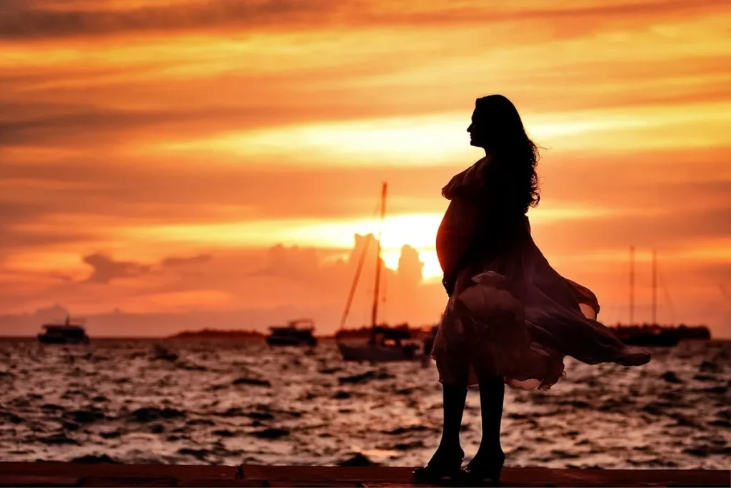 Silhueta de uma mulher grávida em um pôr do sol dramático sobre o mar, simbolizando a esperança e a realização da maternidade através da fertilização in vitro.