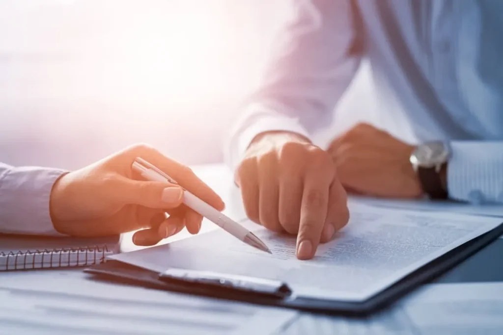 Mãos de dois profissionais apontando para um contrato sobre uma mesa, simbolizando a negociação e assinatura de um acordo de leasing.