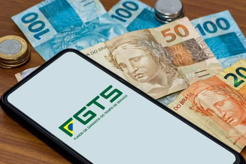 Celular com o aplicativo FGTS aberto sobre notas e moedas de real, representando rendimento e saque.