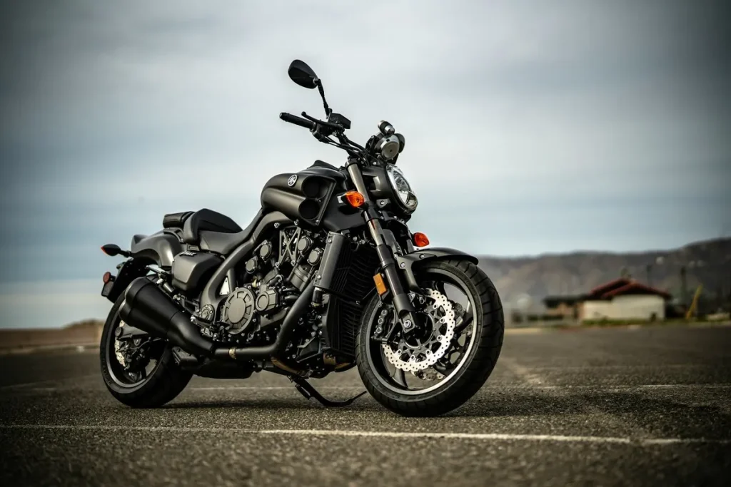 Motocicleta power cruiser preta com design robusto, motor V4 e pneu traseiro largo, estacionada em asfalto com fundo de paisagem montanhosa sob céu nublado.