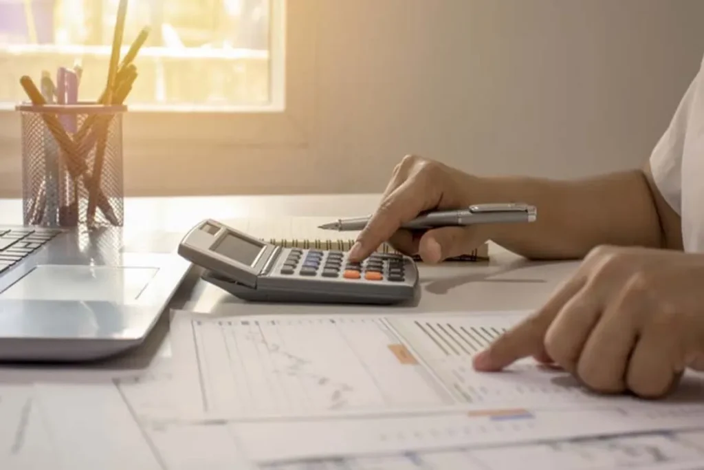 Pessoa usando calculadora e analisando planilhas financeiras para calcular parcelas de compras.