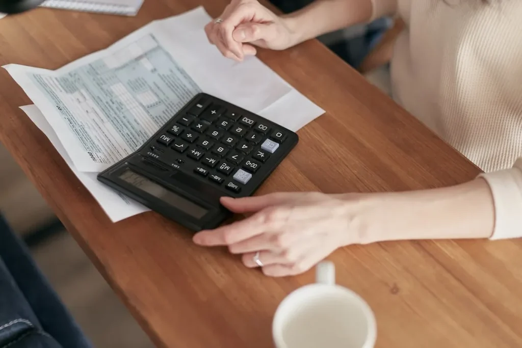 Pessoa usando calculadora sobre documentos financeiros, representando o cálculo de saldo devedor.