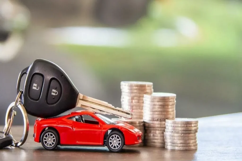 Chave de carro moderna repousando sobre uma miniatura de carro esportivo vermelho, ao lado de pilhas de moedas, simbolizando o custo de propriedade e a desvalorização de um veículo.