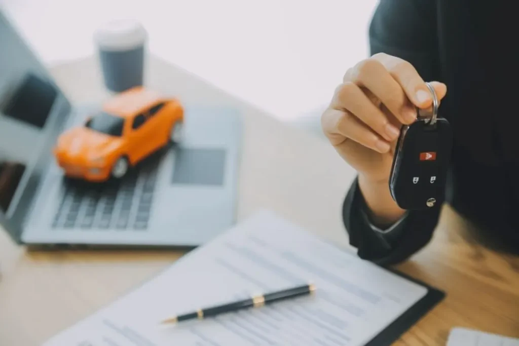 Uma mão segurando as chaves de um carro com uma miniatura de veículo e documentos de financiamento sobre a mesa, simbolizando a quitação da dívida e a retirada do gravame.