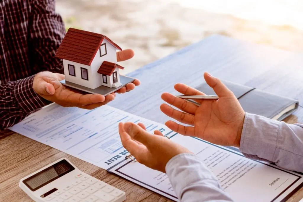Duas pessoas negociando com uma maquete de casa na mão, documentos legais e uma calculadora à frente, representando a complexidade financeira da aquisição de nua-propriedade ou usufruto.