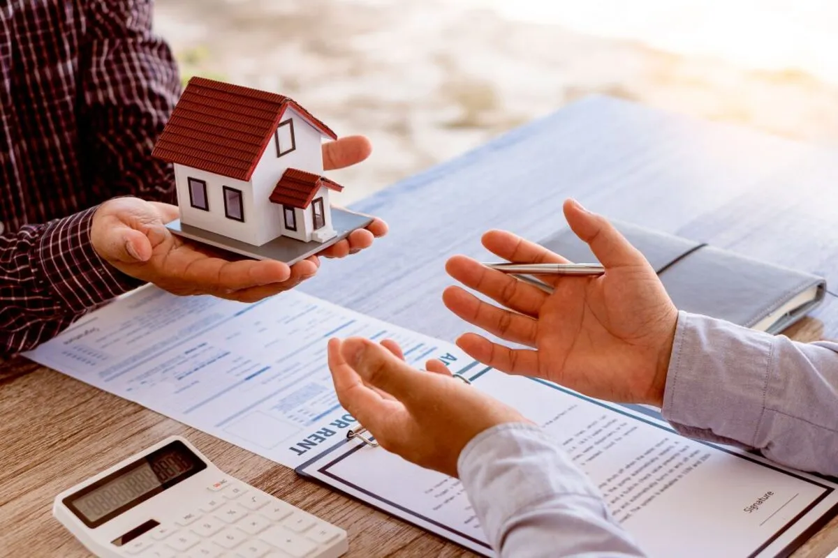 Duas pessoas negociando com uma maquete de casa na mão, documentos legais e uma calculadora à frente, representando a complexidade financeira da aquisição de nua-propriedade ou usufruto.