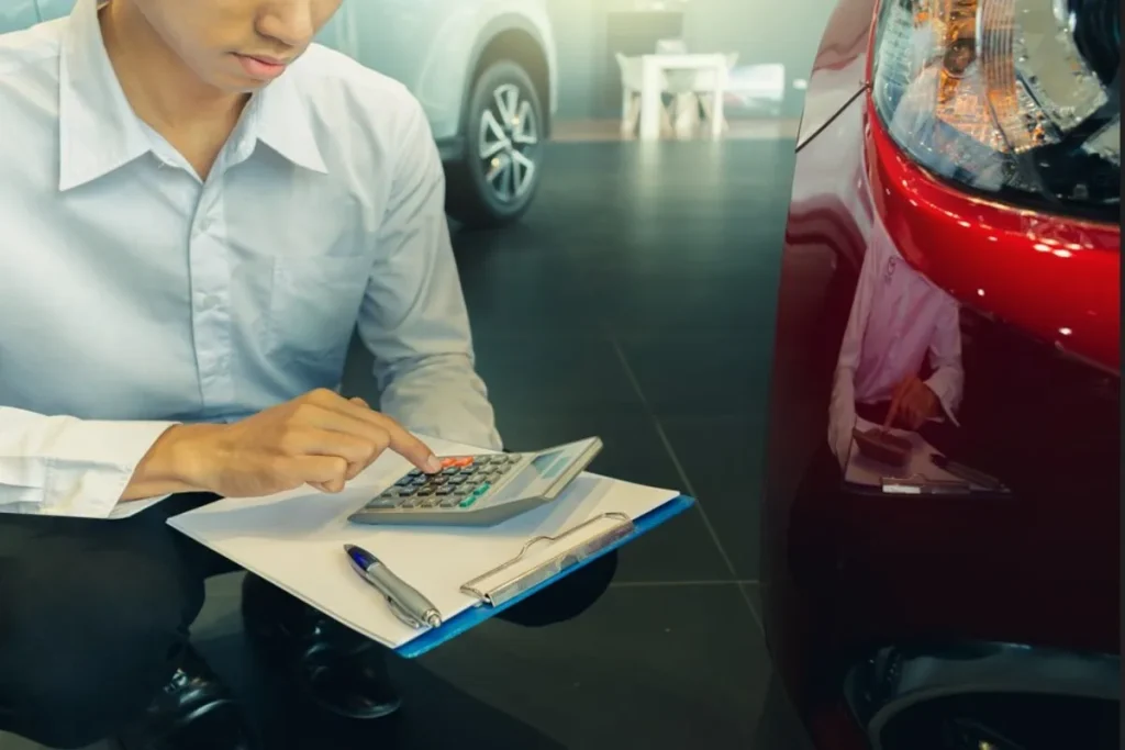 Vendedor ou consultor financeiro usando uma calculadora para mostrar o reajuste ou financiamento de um carro novo vermelho, em uma concessionária.