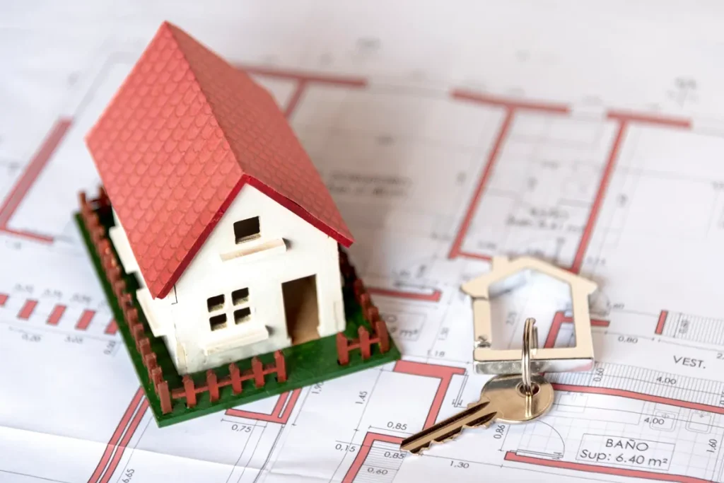 Miniatura de casa com telhado vermelho e chave sobre planta arquitetônica, simbolizando a compra de imóvel com carta contemplada.