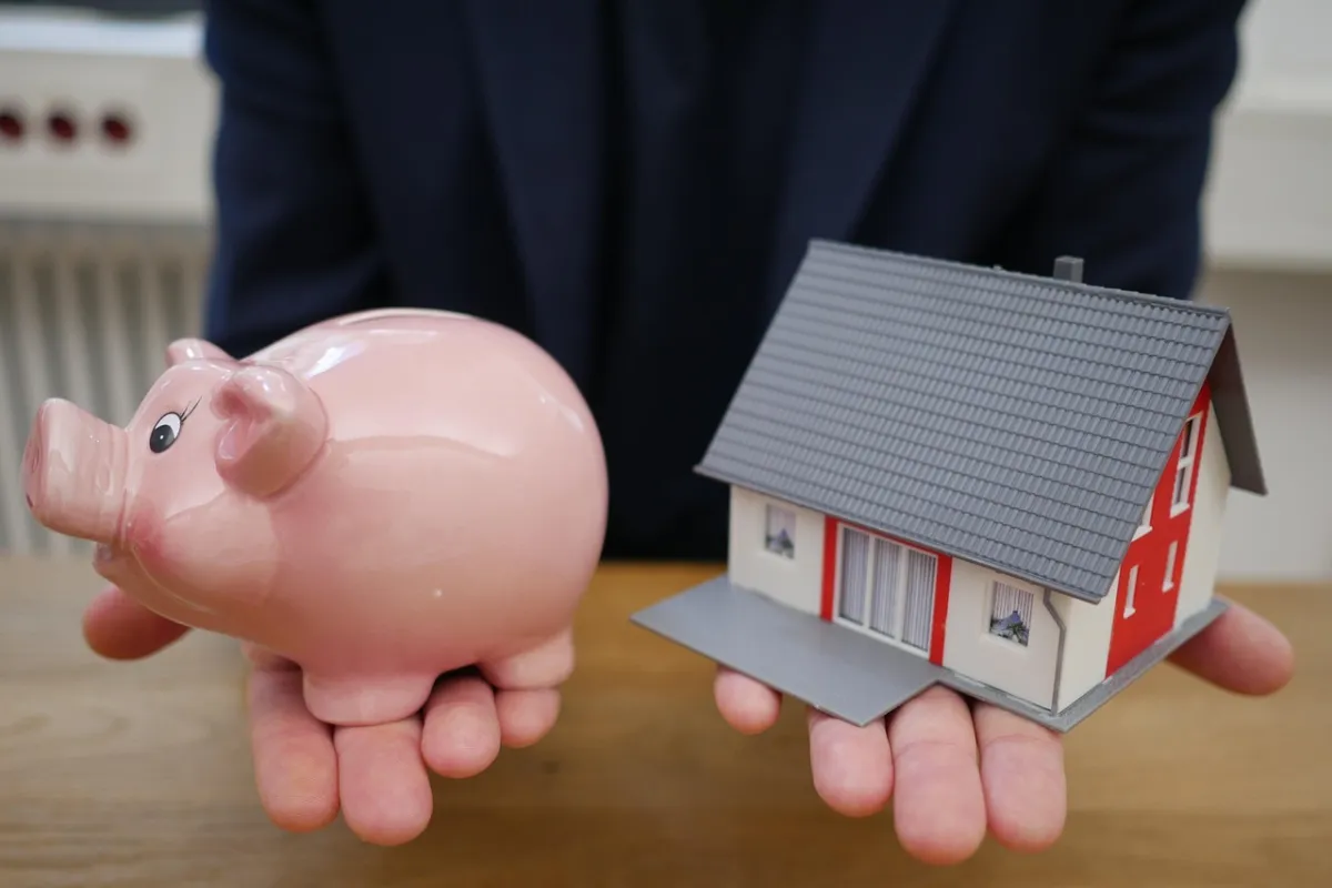 Homem segurando porco e casa em miniatura em cada uma das mãos